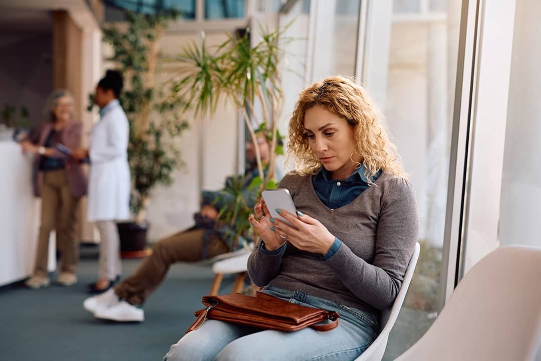 A female patient using her phone while waiting at a clinic for her appointment.
